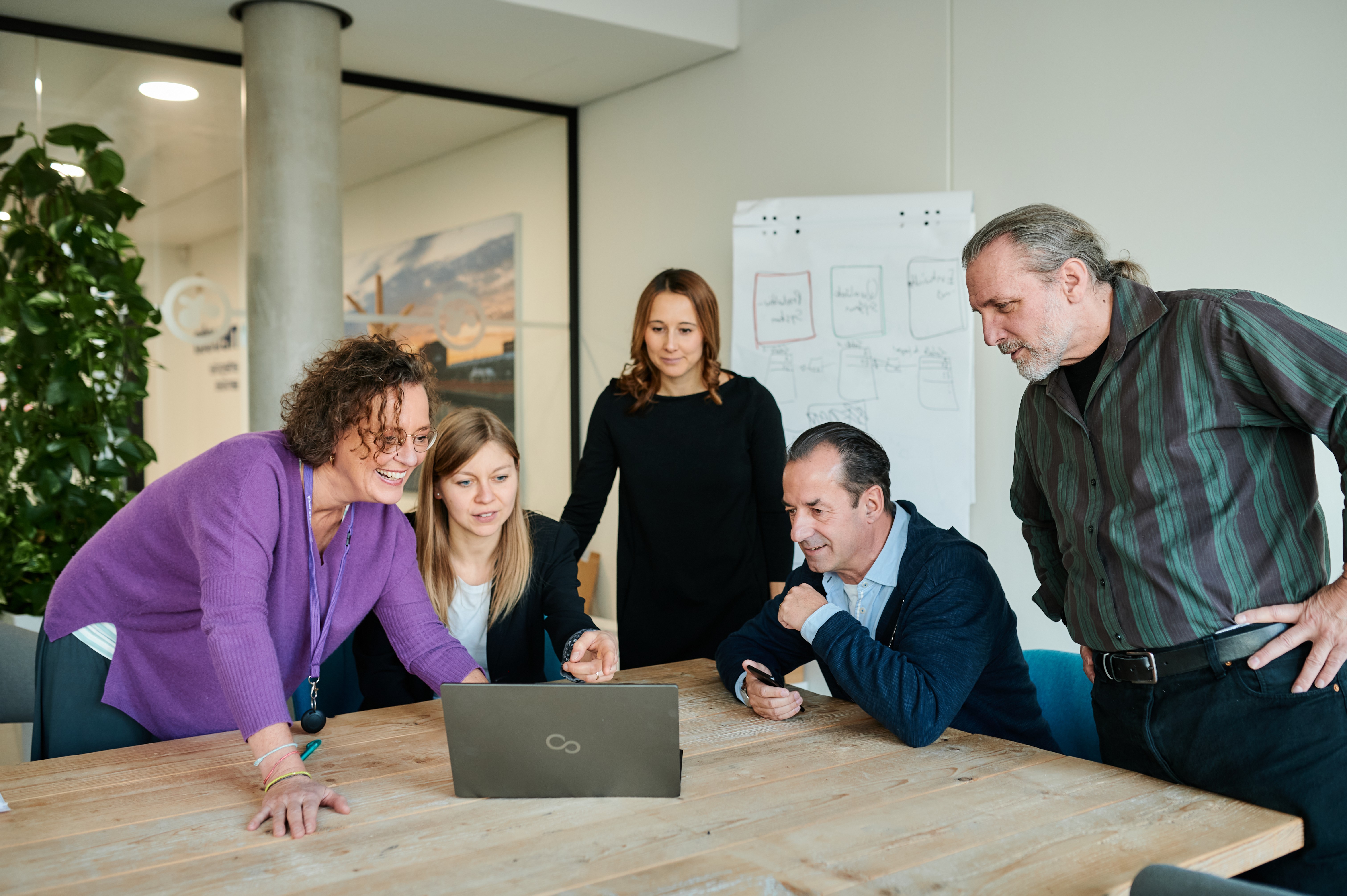 Fünf team neusta Mitarbeitende an einem Tisch vor einem Laptop