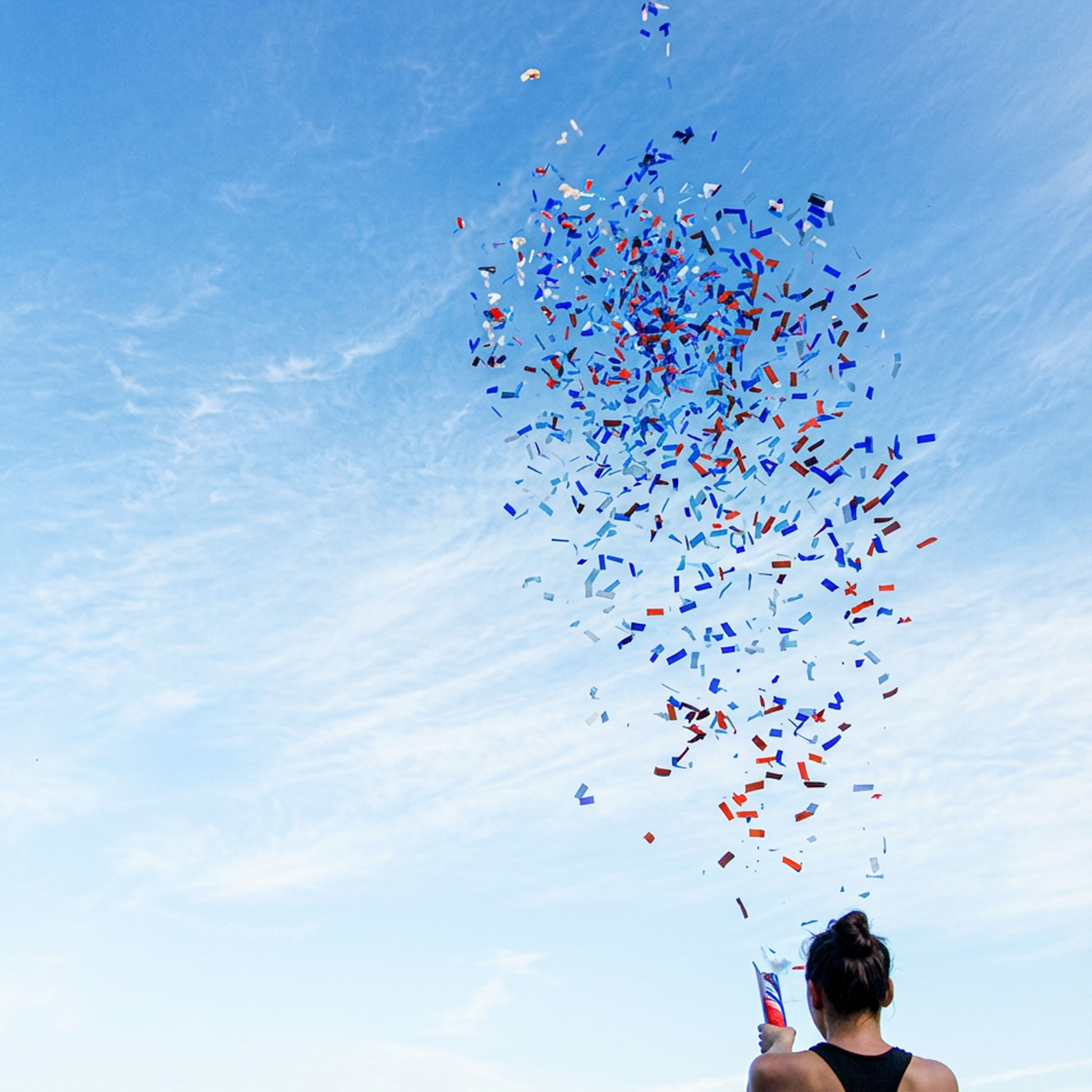 Frau von hinten vor blauem Himmel mit gezündeter Konfettibombe