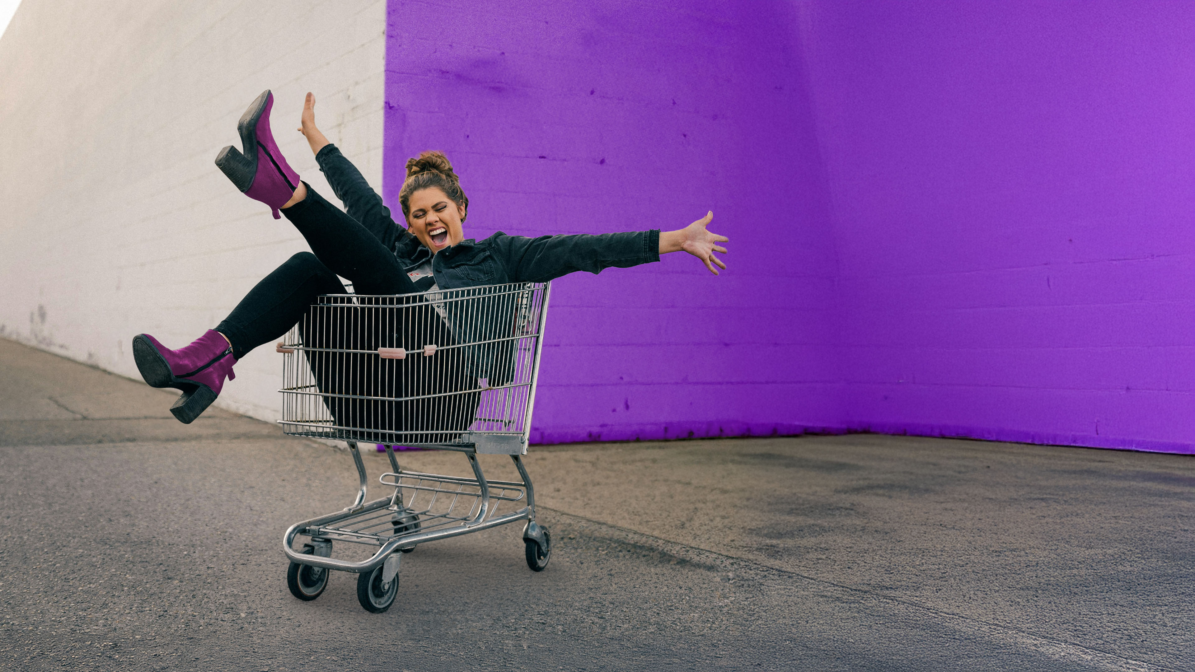 Frau liegt lachend im Einkaufswagen beim Einkaufen