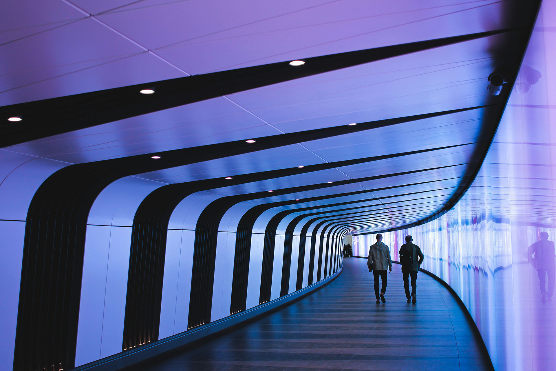 Zwei Personen gehen durch einen modern beleuchteten Tunnel mit blauem Licht