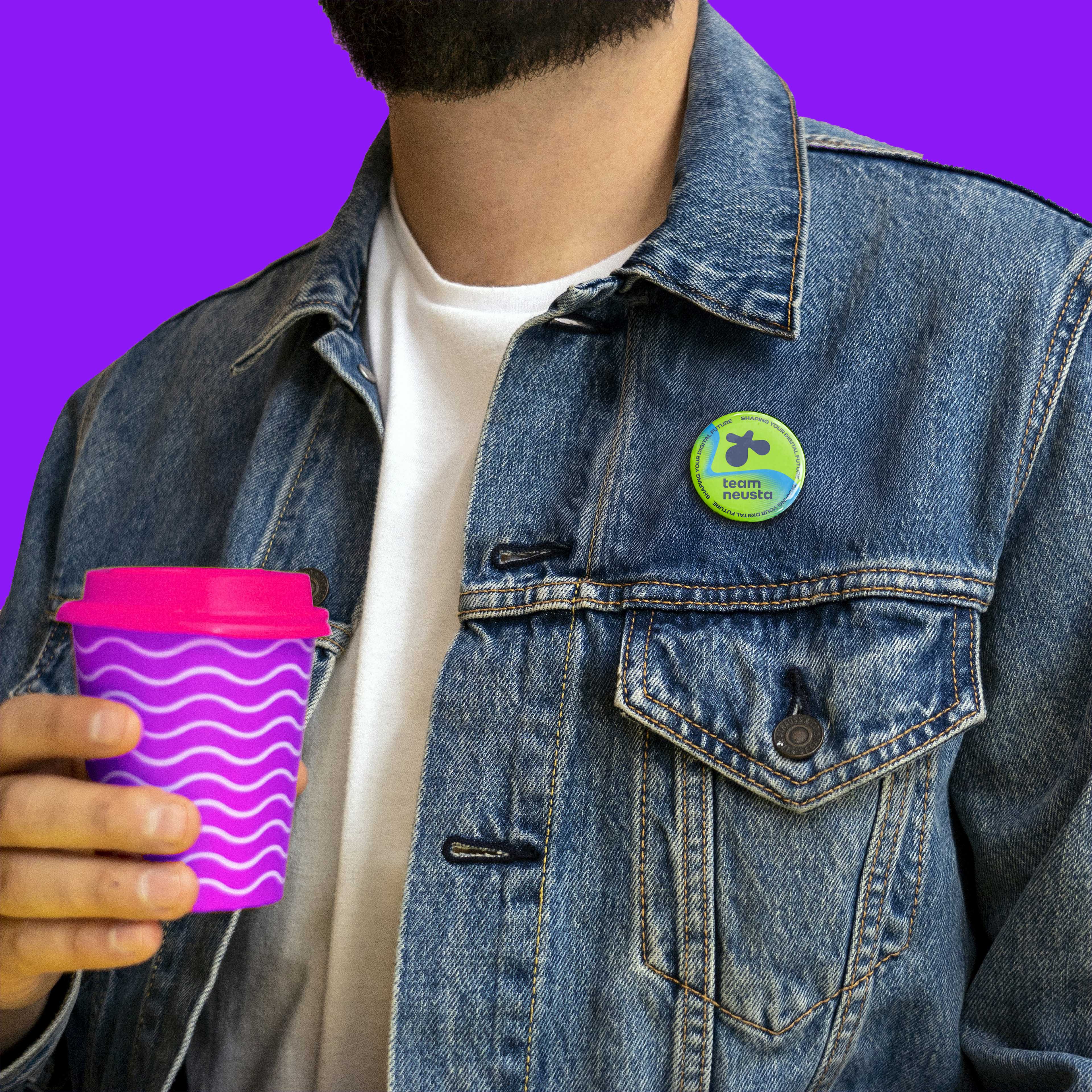 Mann mit Jeansjacke und pinkem Kaffeebecher in der Hand und team neusta Button an der Jacke