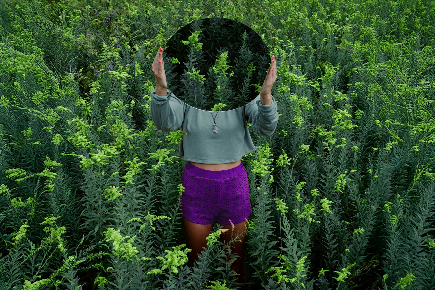 Person steht in dichtem grünem Pflanzenfeld, Gesicht durch Kreis verdeckt