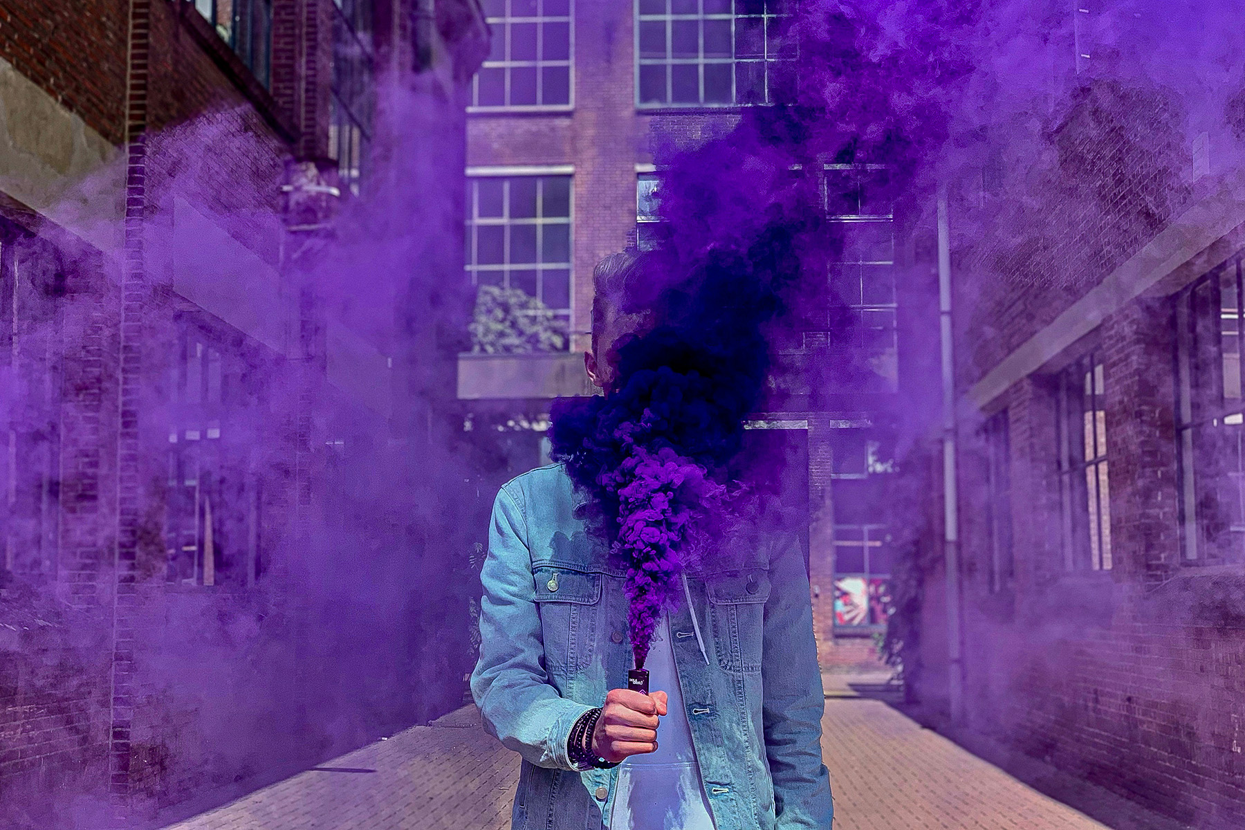 Person hält violette Rauchbombe in einer schmalen Straße zwischen Gebäuden