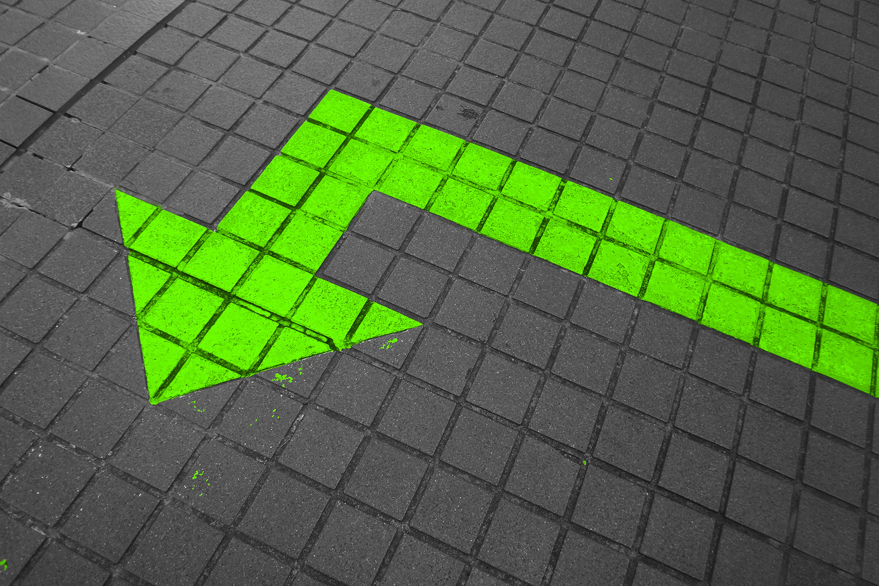 Grüner Pfeil nach Links auf grauen Pflastersteinen