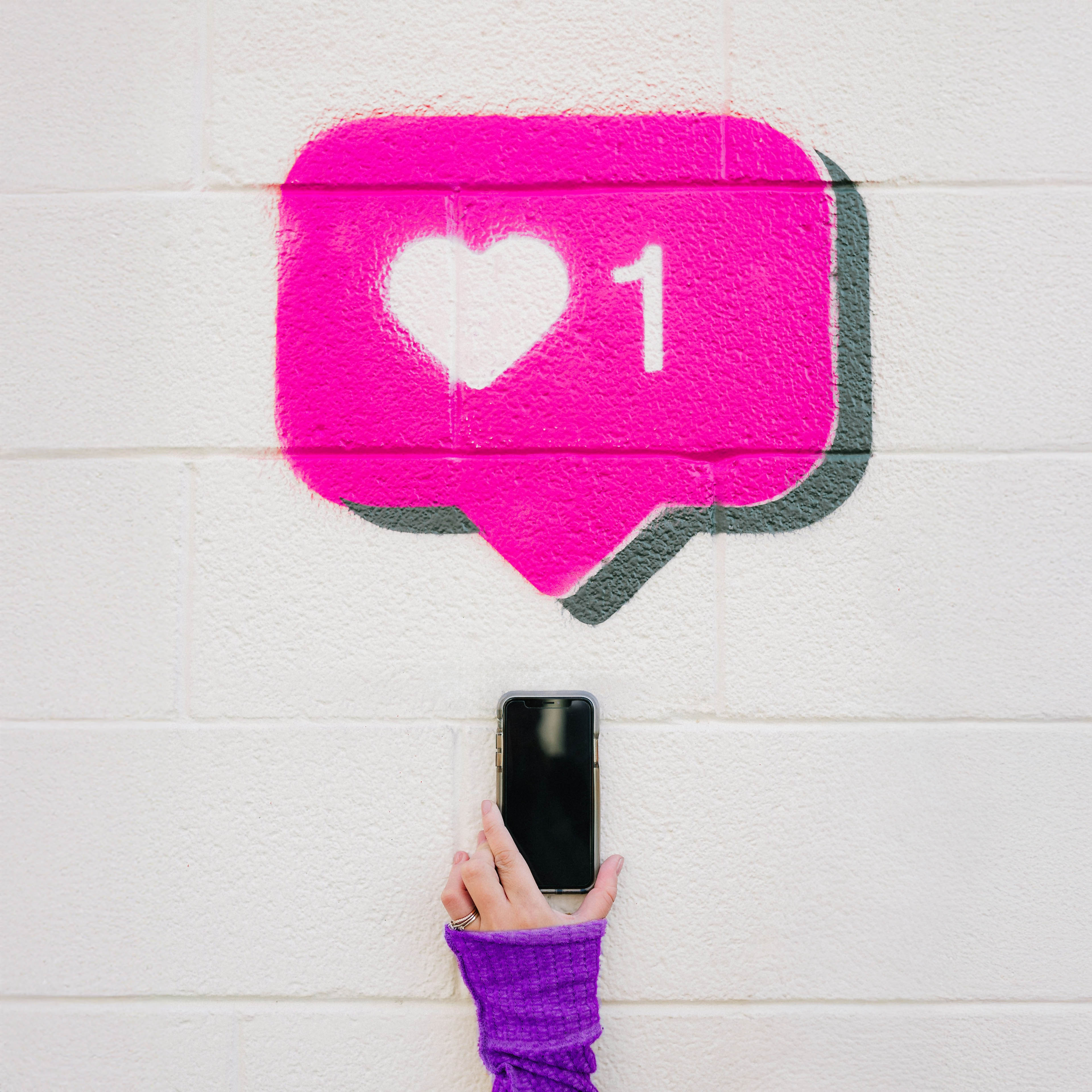 Hand hält Smartphone vor pinkem Graffiti eines Social-Media-Like-Symbols mit Herz