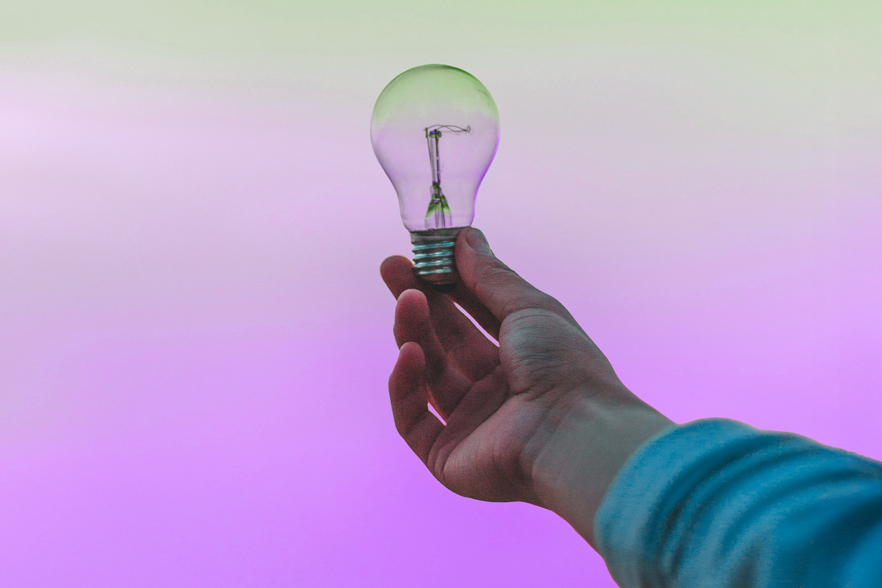 Hand hält Glühbirne vor einem flidafarbenen Himmel